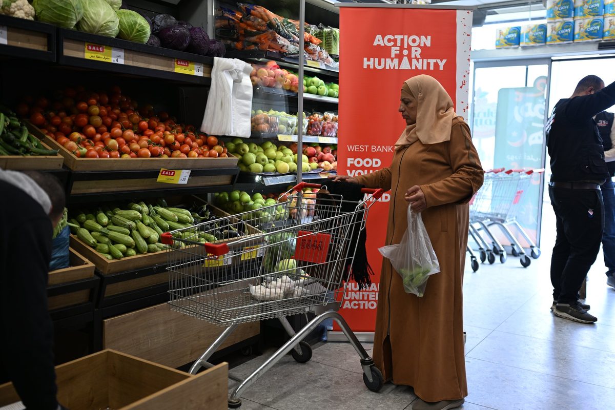 A woman shops for vegetables beside an Action for Humanity banner