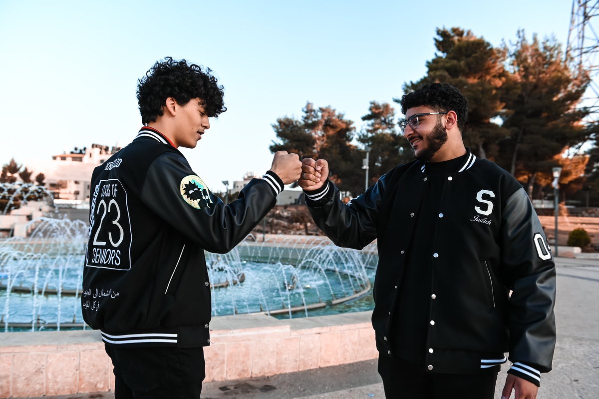 Two young men bump fists in class jackets