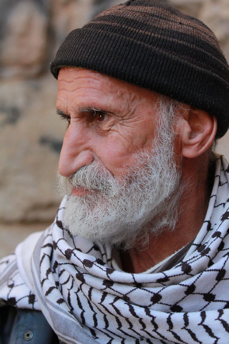 An old man in a black hat and keffiyeh