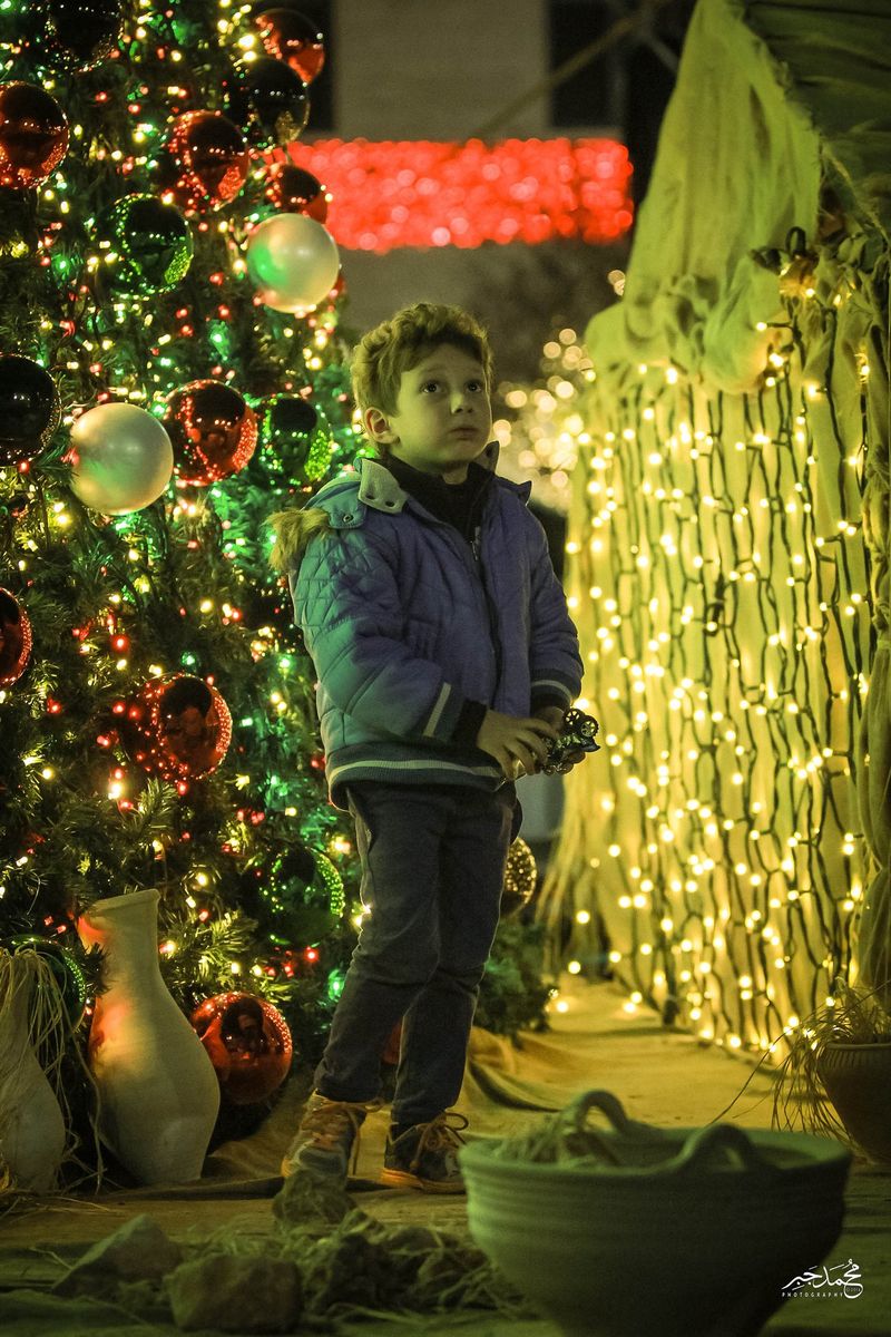 A boy beside a lit Christmas tree at night