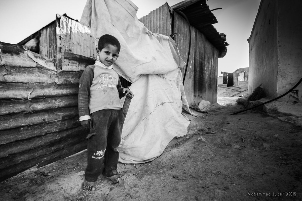 A boy by a tin shack, black and white