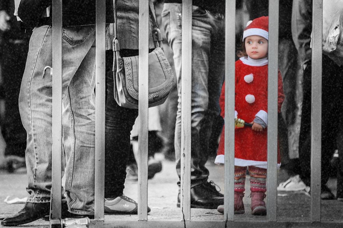 A girl in a Santa dress behind metal railings