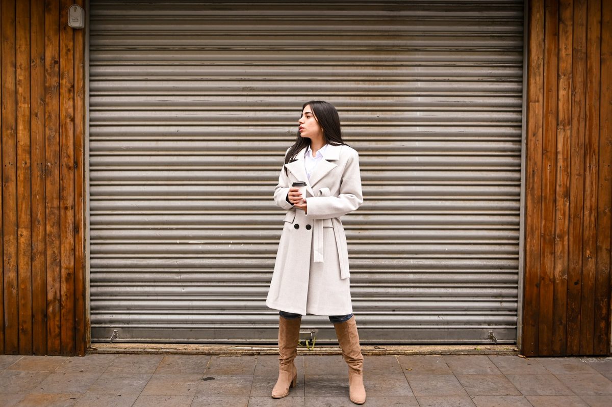 A cream belted coat in front of a wooden shop shutter