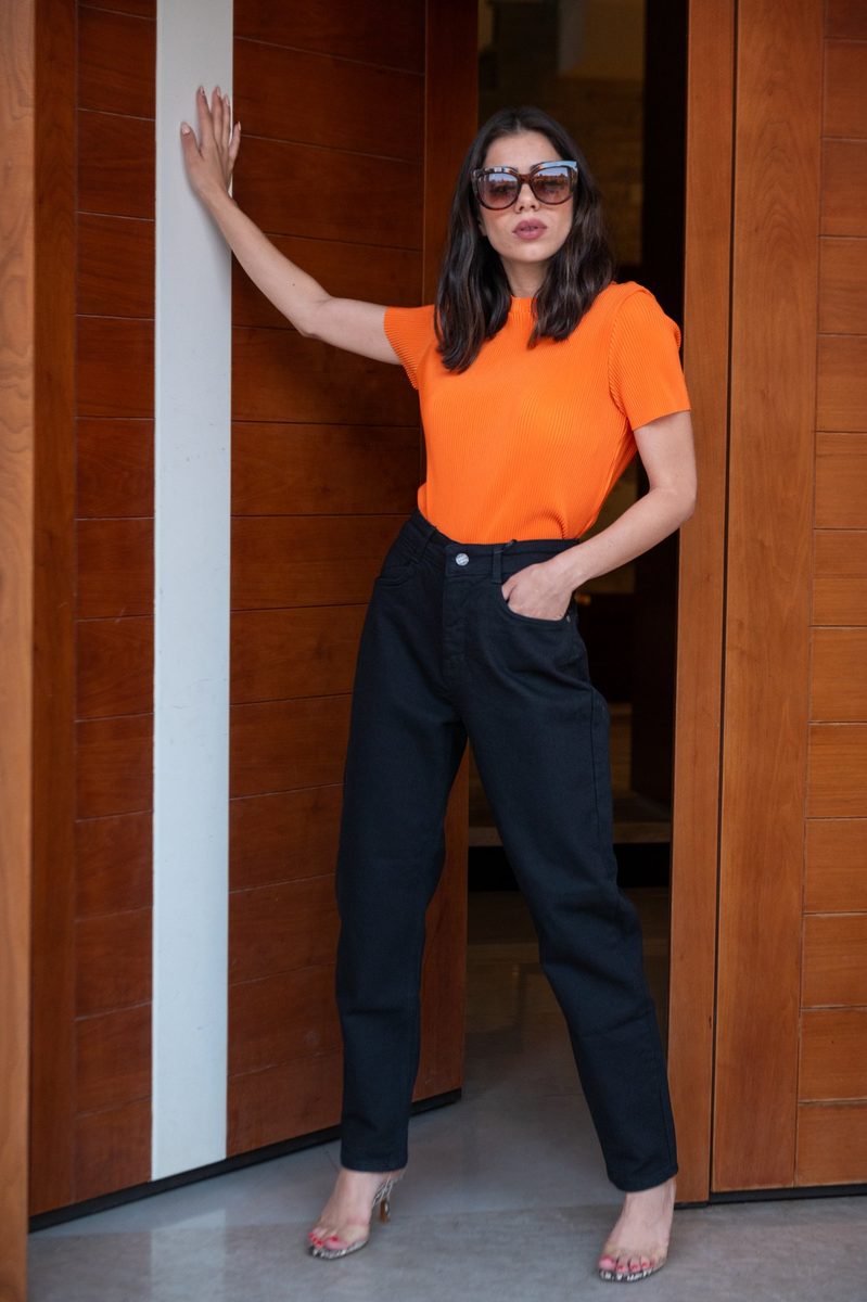 An orange top and black trousers at a wooden door